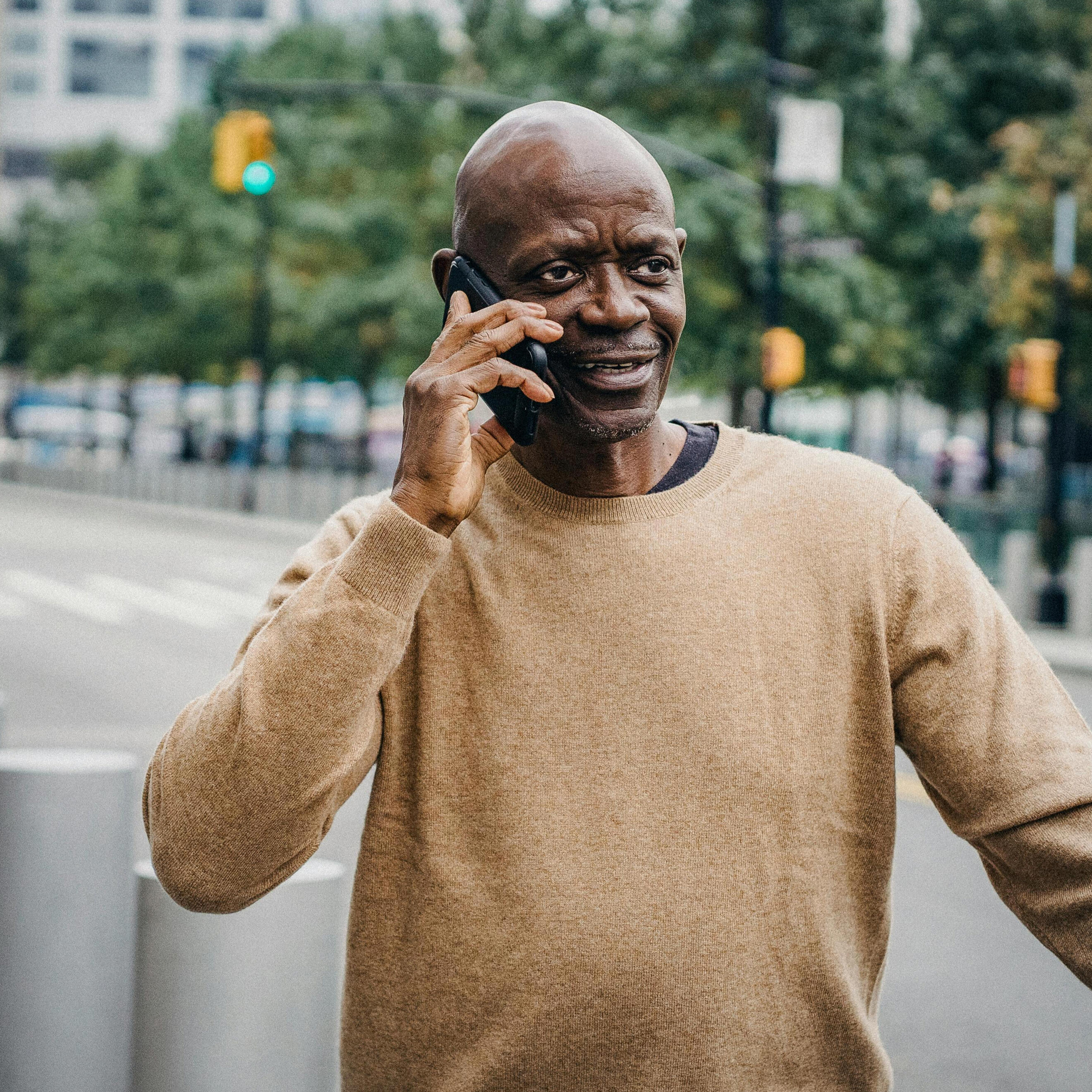 Contact Caleb A man talking on his cellphone while standing on the sidewalk of a city street.