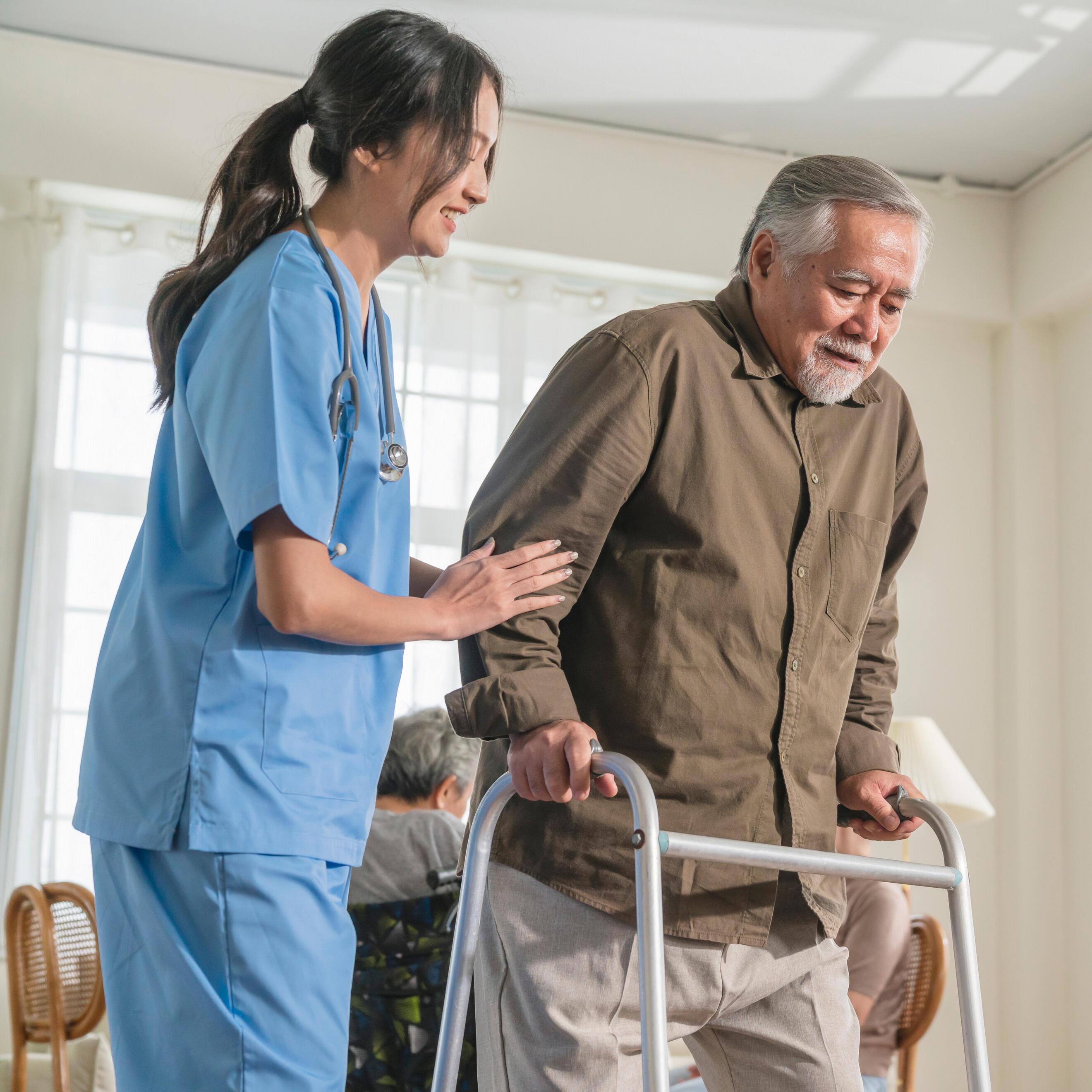 Volunteers of America A woman in scrubs helping an older man using a walker